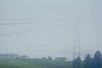 Vista nebbiosa di cavi elettrici e pilone accanto alle case — Foto stock