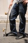 Обрезанное изображение подростка скейтбордиста, стоящего на улице с длинной доской — стоковое фото