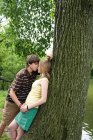Adolescente pareja besándose cerca de árbol - foto de stock