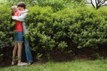 Adolescente pareja besándose en arbusto - foto de stock