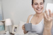 Женщина делает селфи со смартфоном в постели — стоковое фото