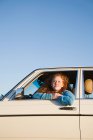 Une jeune femme penchée par la fenêtre d'une voiture — Photo de stock