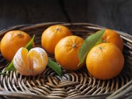 Fruta orgánica fresca, clementinas con hojas en cuenco de mimbre - foto de stock