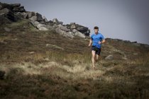 Corredor masculino corriendo desde Stanage Edge, Peak District, Derbyshire, Reino Unido - foto de stock