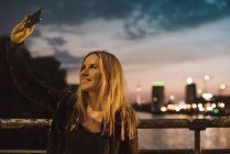 Junge Frau an der Uferpromenade macht Selfie mit Smartphone — Stockfoto