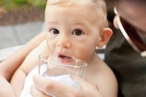 Father helping baby boy drink from cup — Stock Photo