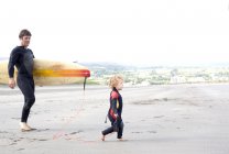 Vater trägt Surfbrett mit Sohn am Strand — Stockfoto