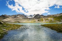 Catena montuosa con fiume sotto cielo nuvoloso blu — Foto stock