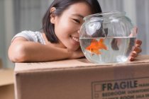 Young woman looking at goldfish on moving box — Stock Photo
