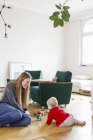 Mid adult woman and baby daughter play with building blocks on living room floor — Stock Photo