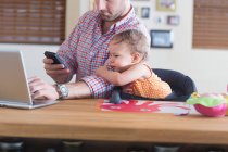 Man working at kitchen counter with baby sitting beside — Stock Photo