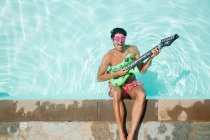 Людина в басейні з надувною гітарою — стокове фото
