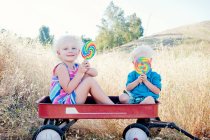Brother and sister sitting in cart with lollipops — Stock Photo