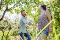 Giovane coppia che si tiene per mano nella foresta scherzando sorridendo — Foto stock