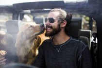 Собака облизує молодого чоловіка бородатим обличчям в джипі — стокове фото