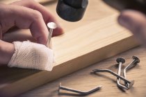 Bandaged finger holding nail on wood — Stock Photo