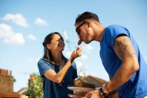 Mid adult woman feeding sausage to boyfriend at rooftop party — Stock Photo