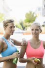 Two young female runners taking a break outdoors with apple and water — Stock Photo
