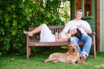 Портрет зрелой пары на скамейке в саду с собакой — стоковое фото