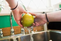 Обрізане зображення дівчини-підлітка, що миє яблуко в кухонній мисці — стокове фото