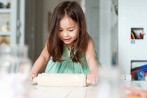 Junges Mädchen rollt Teig auf Küchentheke aus — Stockfoto