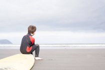 Мальчик сидит на доске для серфинга на пляже — стоковое фото