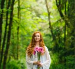 Giovane donna che tiene mazzo di gerbere rosa nella foresta — Foto stock
