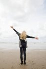 Visão traseira da mulher com braços largos na costa arenosa — Fotografia de Stock