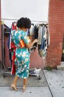 Rückansicht einer jungen weiblichen Modebloggerin mit Afrohaaren, die auf die Kleiderstange am Bürgersteig blickt, New York, USA — Stockfoto