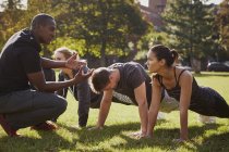 Entrenador personal instruyendo a hombres y mujeres haciendo flexiones en el parque - foto de stock
