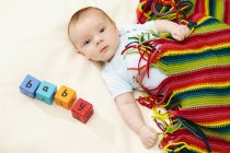 Bébé garçon couché sous une couverture rayée avec des blocs orthographe bébé — Photo de stock
