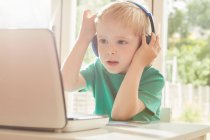 Хлопчик за столом використовує ноутбук і слухає навушники — стокове фото