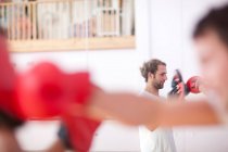Young man and trainer boxing in gym — Stock Photo