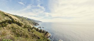 Panoramic view of sun lighted green coastline and sea — Stock Photo