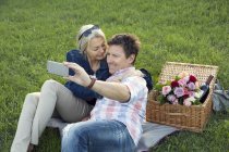 Couple d'âge mûr sur l'herbe ayant pique-nique, prendre selfie — Photo de stock
