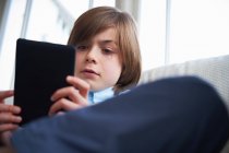 Niño usando tableta digital en el sofá - foto de stock