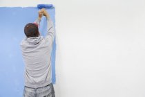 Visão traseira do homem pintura parede azul — Fotografia de Stock