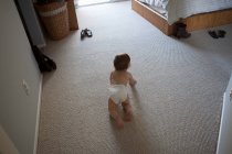 Vista trasera de ángulo alto del bebé niño con pañal arrastrándose en la alfombra en el dormitorio - foto de stock