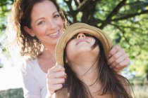 Portrait de femme mature couvrant les yeux des filles avec un chapeau de paille dans le parc — Photo de stock