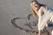 Donna sorridente che scrive messaggio d'amore nella sabbia, Breezy Point, Queens, New York, Stati Uniti — Foto stock