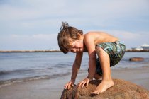 Мальчик приседает на скале на пляже — стоковое фото