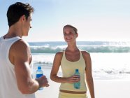 Casal jovem com garrafas de água na praia — Fotografia de Stock