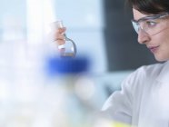 Wissenschaftler betrachten chemische Formel im Becher während Experiment im Labor — Stockfoto