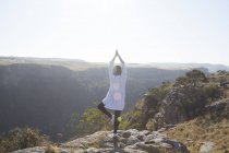 Mujer de pie en la cima de la montaña, en posición de yoga, vista trasera, Sudáfrica - foto de stock