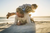 Sons lying on top of father on beach smiling — Stock Photo