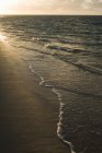 Surf waves on sandy shore during sunset — Stock Photo
