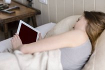 Über-die-Schulter-Ansicht einer Frau, die mit digitalem Tablet im Bett liegt — Stockfoto