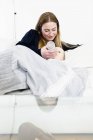 Mulher adulta média mamadeira para bebê filha no sofá — Fotografia de Stock