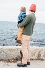Father holding son beside lake, rear view — Stock Photo