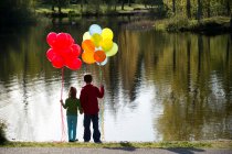 Brother and sister in front of lake with bunches of balloons — Stock Photo